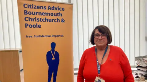 Zoe Bradley from Citizens Advice in her Bournemouth office. She is standing next to a Citizens Advice pop up banner.