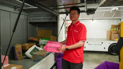BBC/Joyce Liu Man wearing red shirt loads parcel onto the back of a truck