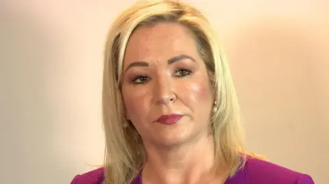 Michelle O'Neill has blonde hair, wearing a purple top.