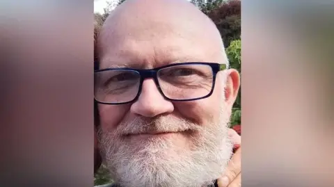 James McKenna. A picture of a bald man with navy blue glasses and a white beard.