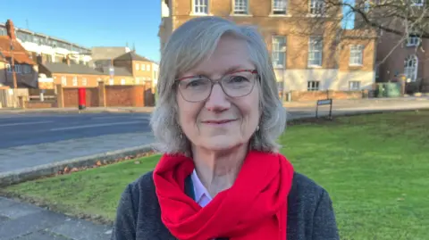 A woman in a red scarf standing outside by some grass and stone office buildings on a sunny day
