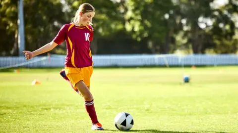 Confident girl kicking soccer ball while practicing in field. Athlete is learning football skills during training. Concept of strength and vitality.