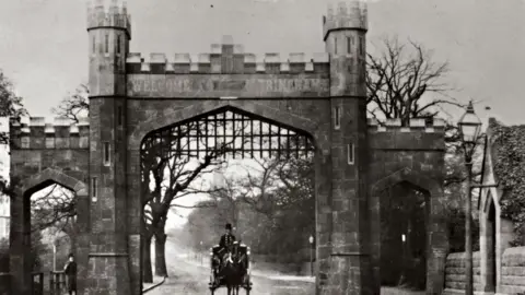 Trafford Council A black-and-white period photograph of Altrincham Arch from Trafford Council's archive. A man on a horse and cart rides under the brick archway. It has two smaller brick arches on either side and a metal gate that has been pulled up. 