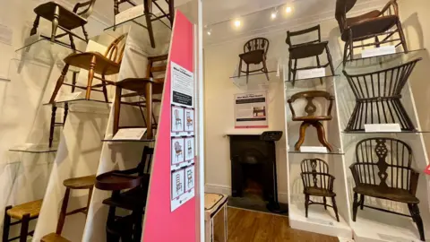 Wycombe Museum A selection of wooden chairs displayed on tiered shelving in a museum 