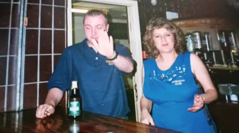 Handout Denise Graham, wearing a blue Unsworth Club apron, with a man. behind the bar, with a man