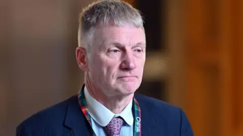 Getty Images A man with grey hair a blue suit and a purple tie and colourful tartan lanyard around his neck