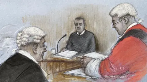 PA Media A court sketch showing John Hunt sitting in a witness box, wearing a dark-coloured jumper and tie, with a stack or folder of papers in front of him. The judge and a barrister are depicted in the foreground