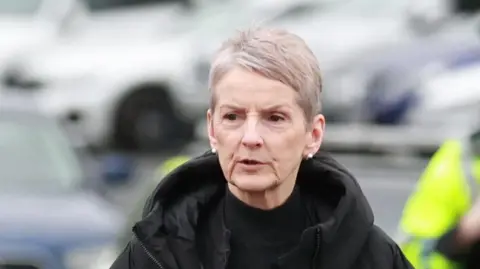 PA Media Lady Eleanor Donaldson arrives at Newry Crown Court.
She has short cropped grey hair and is wearing a black polo neck top, and a black coat with a hood.