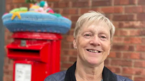 A woman stood near a topped postbox