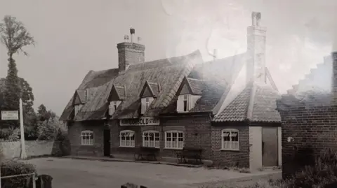 Supplied Picture shows a black and white image of the pub with a thatched roof, a sign advertising Cobbold ales and stout as well as a hanging sign saying Greyhound Inn, Framsden.