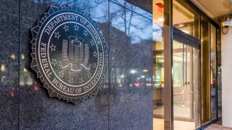 The outside doors of the Department of Justice, Federal Bureau of Investigations is seen from outside. The insignia says the name of the department and decorated with stars around a coat of arms.