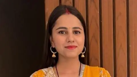 Family Harshita Brella wearing a yellowish  saree looking astatine  the camera and smilling