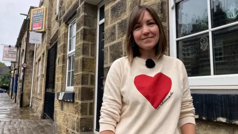 BBC/Carla Fowler A woman in a sweater standing on a street looking at the camera