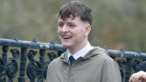 Spindrift Ciaran Wason wearing a shirt, tie and grey/green jacket. He has short, brown hair and is smiling.