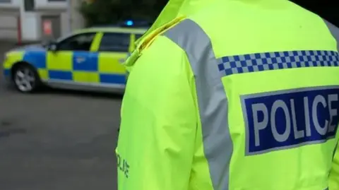 Police officer in hi-vis jacket taken from the back with a police car in the background