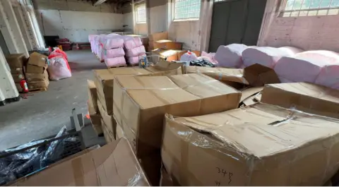 Large numbers of boxes inside a warehouse - alongside dinghies and lifejackets in plastic bags