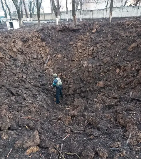 Reuters A member of the Ukrainian emergency services examines a large bomb crater at the Mariupol children's and maternity hospital - 9 March 2022