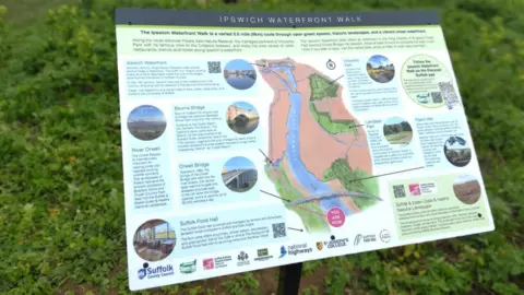 Suffolk County Council An information board which has the words Ipswich Waterfront Walk on the top of it and a large graphic showing the route of the walk, flanked by circular images of a variety of different locations on the route. Next to the images are paragraphs of information about each destination.
