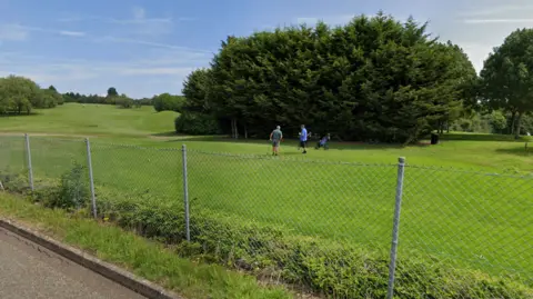 Golfers on a fairway behind a mesh fence