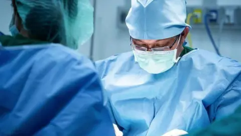 Surgeons operating in a theatre, wearing blue scrubs and masks