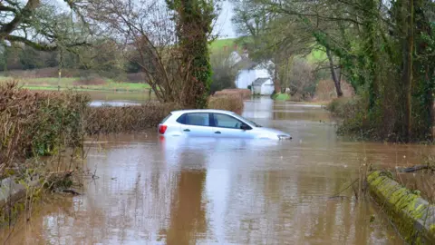 warren weatherman A silver car submerged in flood water in Devon.