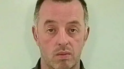 West Yorkshire Police Mugshot of Martin Bell. He has grey stubble, grey hair and a long face.
