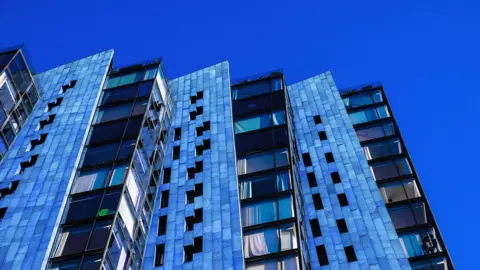 A block of blue flats in Manchester, England pictured against a bright blue sky.