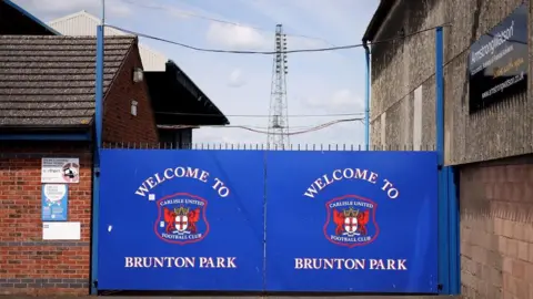 Getty Images Afuera de Brunton Park hay una gran puerta azul con la insignia roja de Carlisle United que dice 