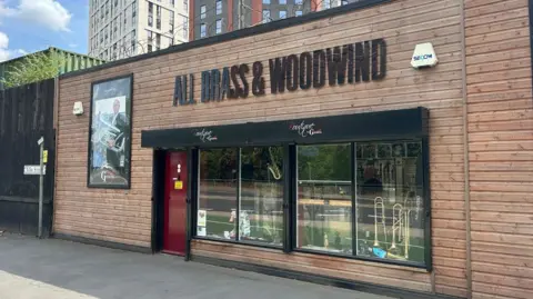 Amy Monkman/BBC A brass and woodwind shop which is clad in wood and has a black sign 