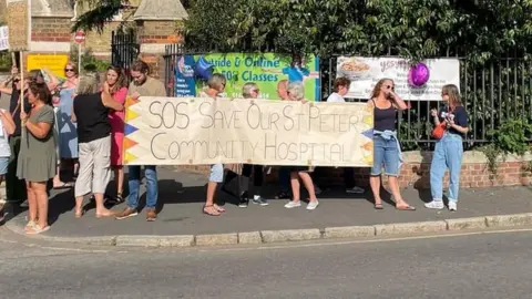 A protest at St Peter's Hospital, with people holding a large placard.