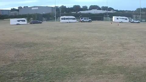 A CCTV image of three cars each towing caravans across a sports field.
