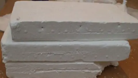 Norfolk Police Three rectangular blocks of white cocaine, piled up one on top of the other. They are resting on a wooden table. 