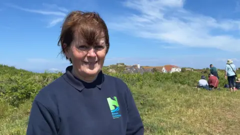 A woman standing on L'Ancresse Common, smiling at the camera