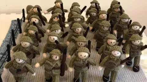 The Longest Yarn A group of 29 crocheted soldiers. They are wearing army uniforms and carrying packs and guns.