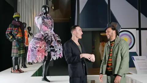 Julie Howden Mannequins dressed in couture by designers Charles Jeffrey and Nicholas Daley who stand to the right of the mannequins.