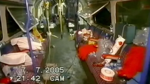 The inside of a London underground tube, showing the aftermath of the terror attacks on the 7th of July, 2005. The windows are smashed and the carriage is empty, with piles of debris on the seats.