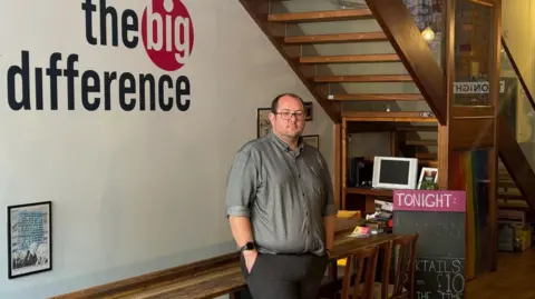A man in a shirt stood in front of a wall painted with the words "The Big Difference" 