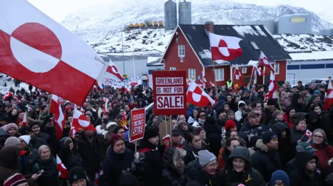 People hold Greenlandic flags and placards as they gather by the United States Consulate to march in protest against U.S. President Donald Trump and his announced intent to acquire Greenland.