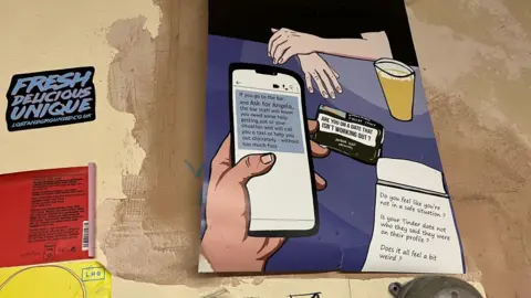 BBC An 'Ask for Angela' graphic poster on the wall behind the bar at Kongs in Bristol