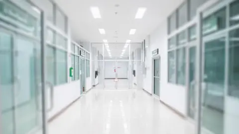 Getty Images Image shows clear doors opened on the left and right of the picture showing a hospital corridor with a white floor, walls and ceiling with glass doors on the left and right 
