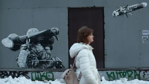 Getty Images A woman walks in front of the graffiti depicting a Ukrainian serviceman making a shot with a US-made Javelin portable anti-tank