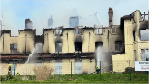 The shell of the council offices in Sidmouth following a fire - with firefighters hosing down what is left of the building