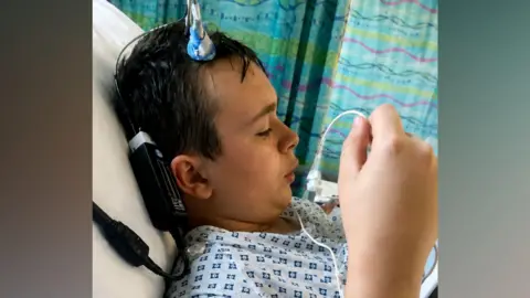 PA Real Life A young man lying in a hospital bed with several nodes attached to him.