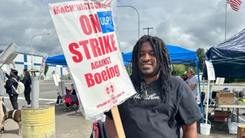 BBC Davon Smith in piedi sul picchetto, con in mano un cartello che dice "Il sindacato dei macchinisti in sciopero contro la Boeing"