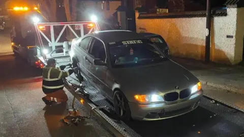 BBC An image of a BMW car being taken away on a trailer after being seized by police.