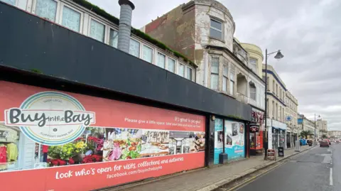 LDRS A rundown shop frontage with a sign urging people to "buy in the Bay" 