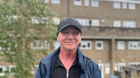 Eden Hannigan/BBC Robert Dawson in a baseball cap smiling with flats in the background