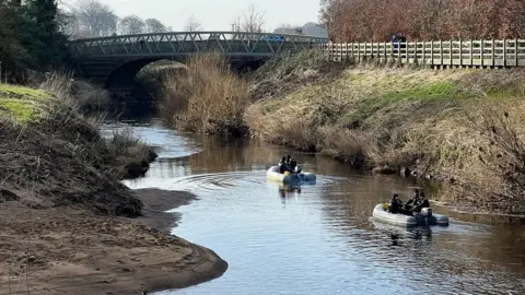 A river with two small search boats with specialist officers. A bridge in the background.