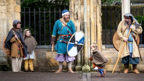 Danny Lawson/PA Wire Viking re-enactors during the Jorvik Viking Festival in York. A little boy runs along the road in front of medieval walls. A woman and a girl stand at the left and a man stands in the middle - they are all in costume