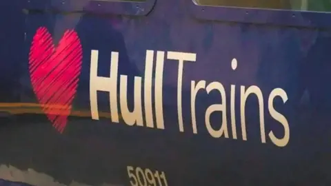 A close-up of the side of a dark blue train carriage with a large logo reading "Hull Trains" in white text, next to a pink heart. A train serial number reads "50911".